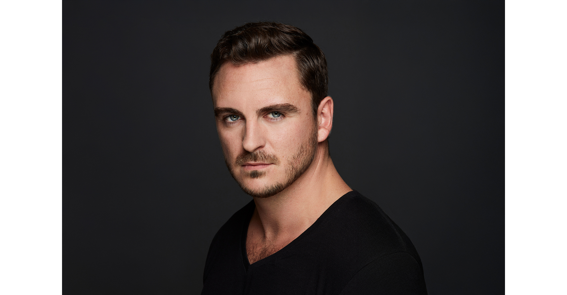 dark haired actor in front of a dark grey painted backdrop